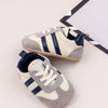 A pair of baby first walker shoes featuring a light gray canvas upper with navy blue stripes and an anti-slip TPR sole.