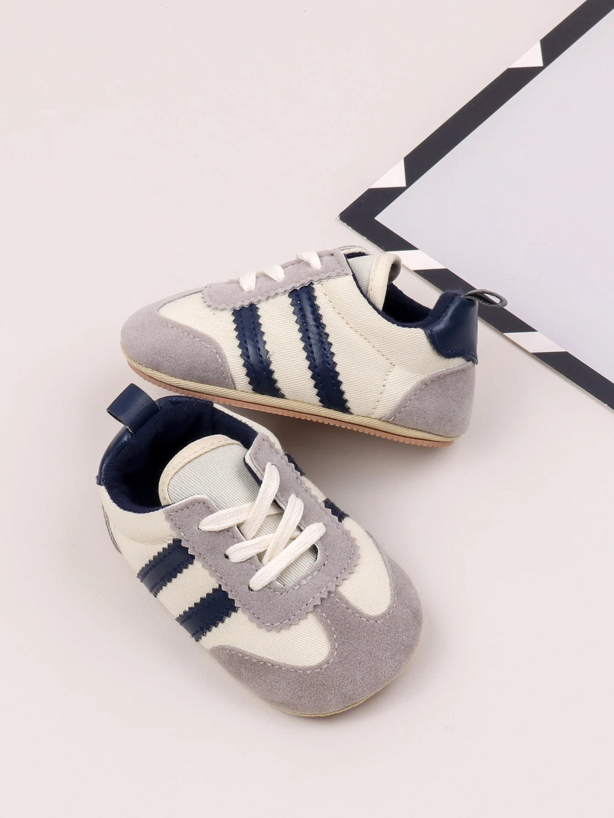 A pair of baby first walker shoes featuring a light gray canvas upper with navy blue stripes and an anti-slip TPR sole.