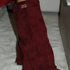 A close-up of a maroon knee-high boot with a chunky heel and a gold metal buckle.