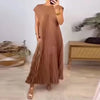 A woman wearing a long, pleated, sleeveless midi dress in a brown color standing indoors.