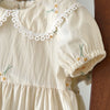 A light cream girls summer dress with floral embroidery and delicate white lace trim on the neckline and sleeves.