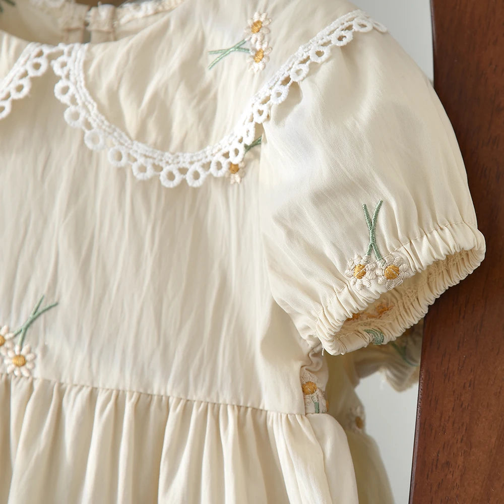 A light cream girls summer dress with floral embroidery and delicate white lace trim on the neckline and sleeves.