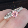 Nærbilde av en sølvforlovelsesring med en rund rosa edelsten omgitt av briljantdiamanter.