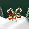 Broche navideño en forma de campana con esmalte rojo y blanco a rayas y detalles dorados, sobre nieve.