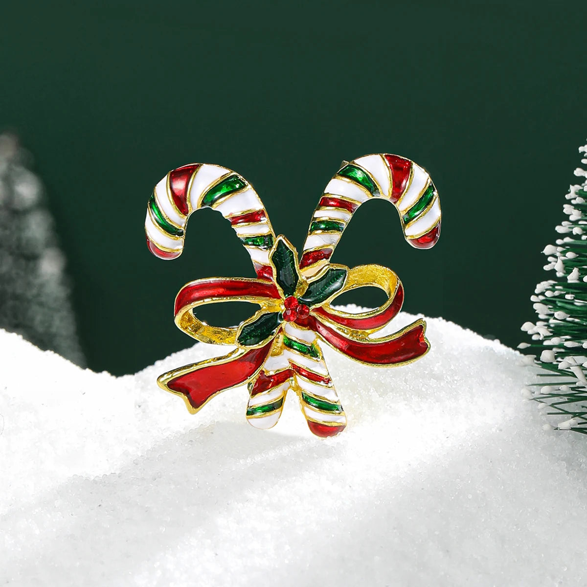 Broche navideño en forma de campana con esmalte rojo y blanco a rayas y detalles dorados, sobre nieve.
