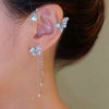 A close-up of a woman's ear adorned with a sparkling butterfly flower ear cuff and dangling crystal drops.