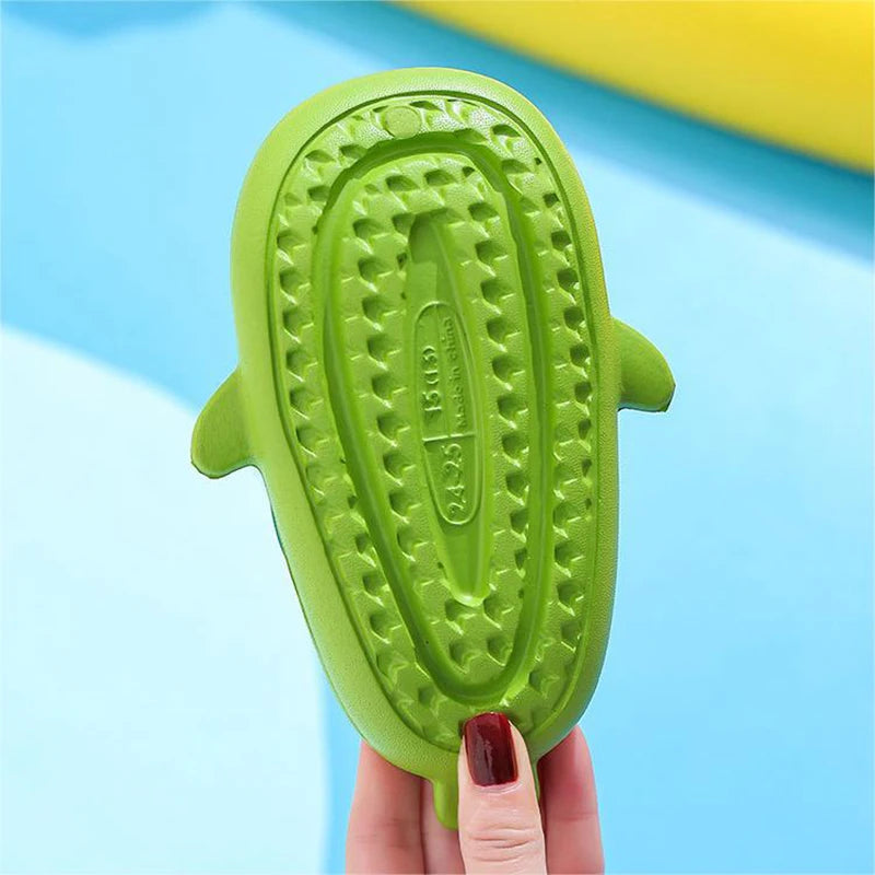 A bright green kids shark clog sandal with a textured anti-slip sole being held by a hand.