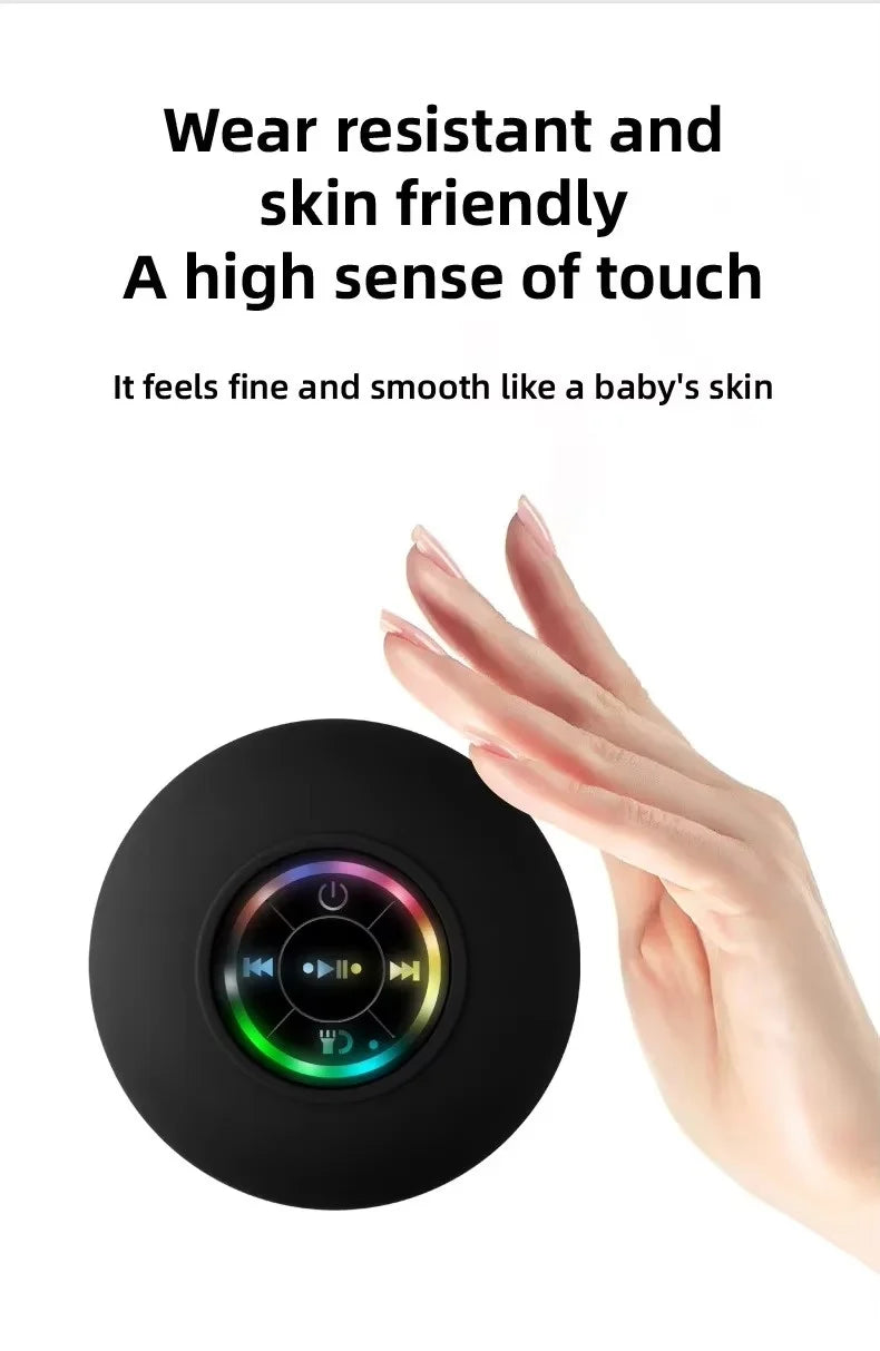 A hand is holding a black compact waterproof Bluetooth speaker with a suction cup mount.