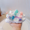 A hand holds a pair of pink and teal breathable princess sandals for summer.