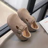 A pair of tan suede kids' moccasin shoes with an easy hook-and-loop closure resting on a gray surface.