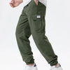 A man wearing olive green cargo joggers and a white shirt, featuring a small embroidered logo on the pocket.