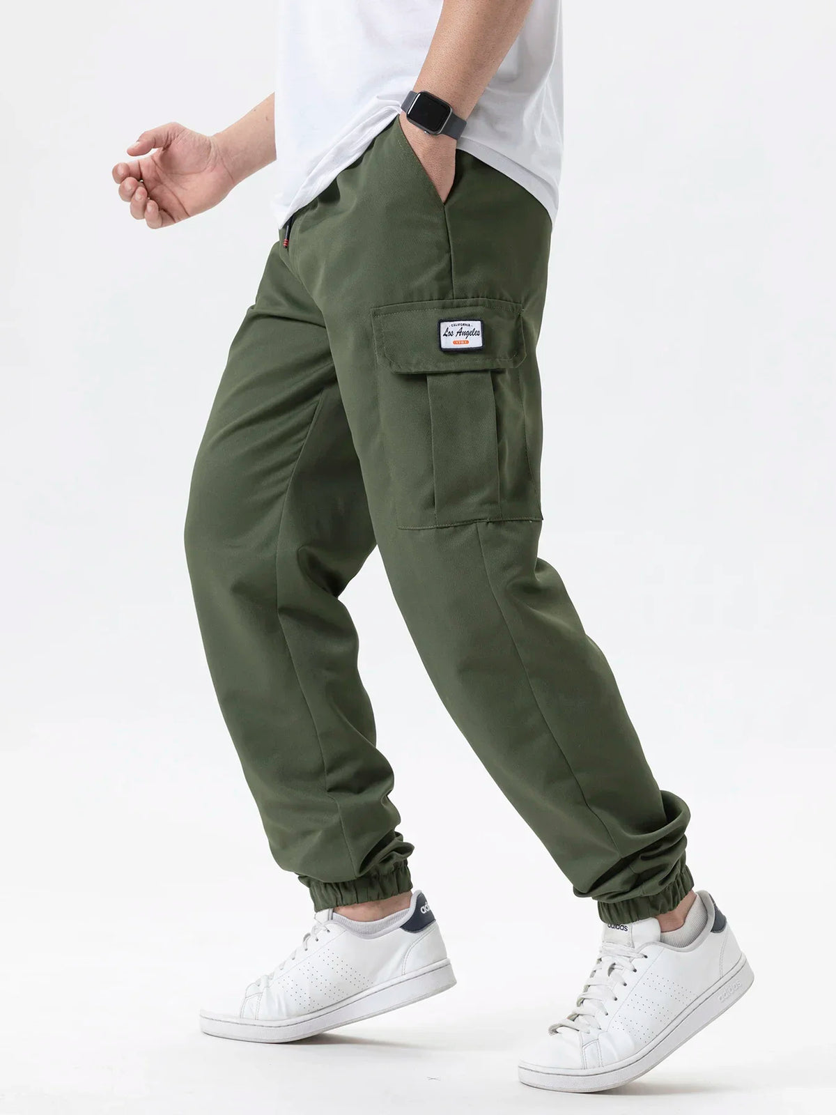 A man wearing olive green cargo joggers and a white shirt, featuring a small embroidered logo on the pocket.