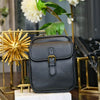 Black vegan leather messenger bag with gold hardware displayed on a marble surface.