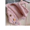 A pink knitted cardigan sweater for girls with a textured knit and pom-pom trim draped over a light-colored surface.