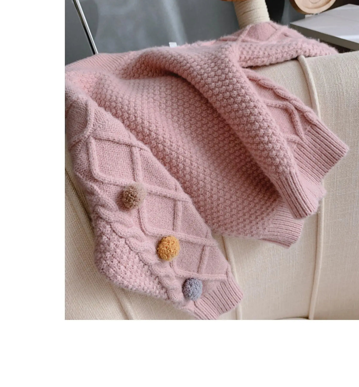 A pink knitted cardigan sweater for girls with a textured knit and pom-pom trim draped over a light-colored surface.