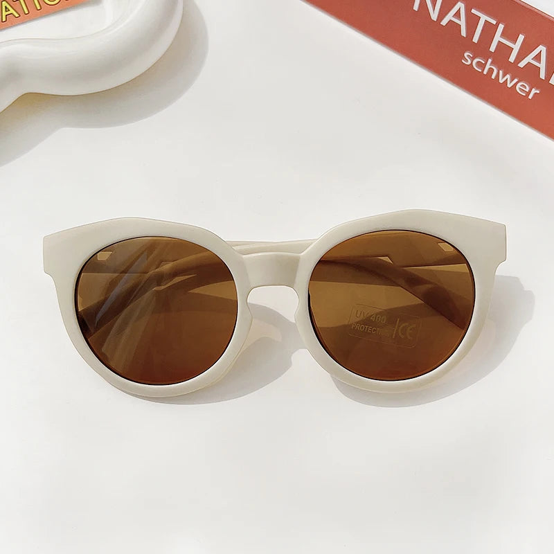 A pair of white sunglasses with brown tinted lenses resting on a white surface.