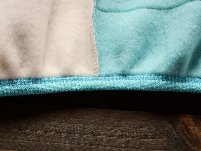 A close-up of a light beige and teal fleece pajama set with ribbed trim on the neckline.