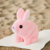 A pink plush rabbit toy sitting on a white surface against a sandy background.