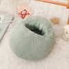 A round, light green fleece foot warmer with a soft inner lining rests on a white textured surface.