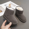 A close-up of a gray kids winter ankle boot with a plush white lining being held by a hand.