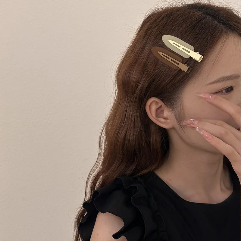 A close-up of a woman with long brown hair wearing two matte resin side hair clips on the side of her head.