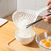 A hand is using a long-handled kitchen strainer spoon to lift shredded white food from a bowl onto a wooden board.