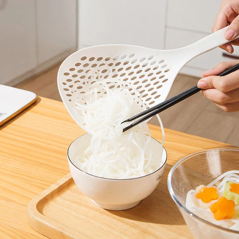A hand is using a long-handled kitchen strainer spoon to lift shredded white food from a bowl onto a wooden board.