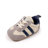 A pair of baby first walker shoes with light beige canvas and navy blue stripes and a dark sole.