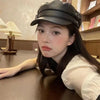 A young woman wearing a black PU leather beret hat sitting at a wooden table.