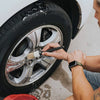 A hand is using a brush to clean the rim of a tire on a car wheel.
