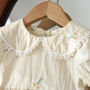 A cream-colored girls summer dress with delicate white lace trim and small floral embroidery on the neckline.