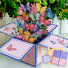 A pink and purple 3D pop-up love tree card featuring a couple silhouette surrounded by colorful flowers.