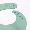 A light green silicone baby bib with a catch pocket and small holes for fastening.
