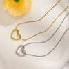 A dainty gold heart pendant necklace with a snake chain displayed on a white surface next to a yellow flower.