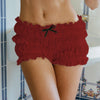 A close-up of a woman wearing red ruffled tiered shorts with a black bow detail.