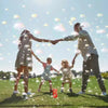 A family of four is outdoors holding hands while blowing bubbles in the air.