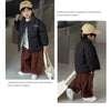 A boy wearing a black quilted winter jacket and brown pants with a light beige hat.