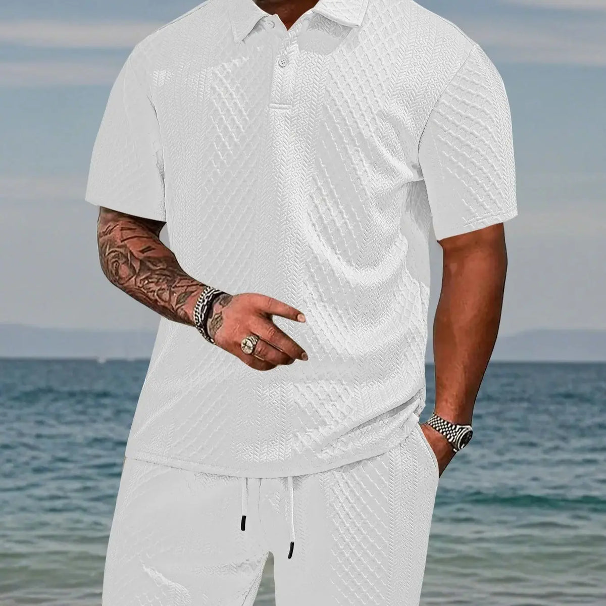 A man wearing a white jacquard short-sleeve shirt and matching drawstring shorts by the sea.
