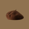 A close-up view of a brown wool beret hat resting on a plain tan background.