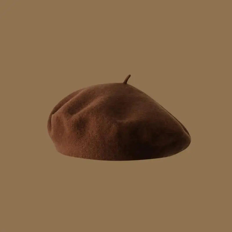 A close-up view of a brown wool beret hat resting on a plain tan background.