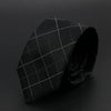 Corbata negra con patrón de cuadrícula blanca, doblada sobre una superficie oscura.