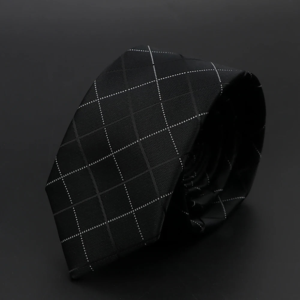 Corbata negra con patrón de cuadrícula blanca, doblada sobre una superficie oscura.