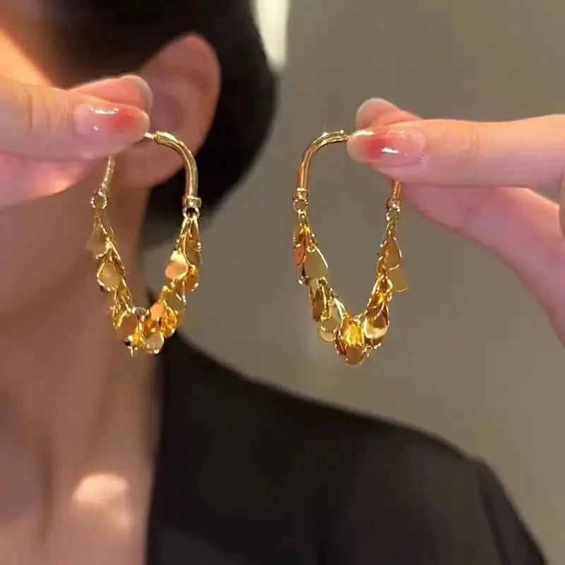 A pair of gold geometric tassel drop earrings being held up by a person's fingers.