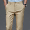 A pair of beige men's stretch straight-leg trousers paired with a light blue shirt and a wristwatch.