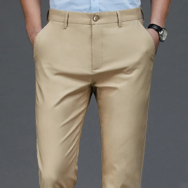 A pair of beige men's stretch straight-leg trousers paired with a light blue shirt and a wristwatch.