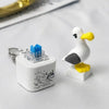 A white seagull-shaped fidget toy with yellow beak and feet, next to its blue keychain component.