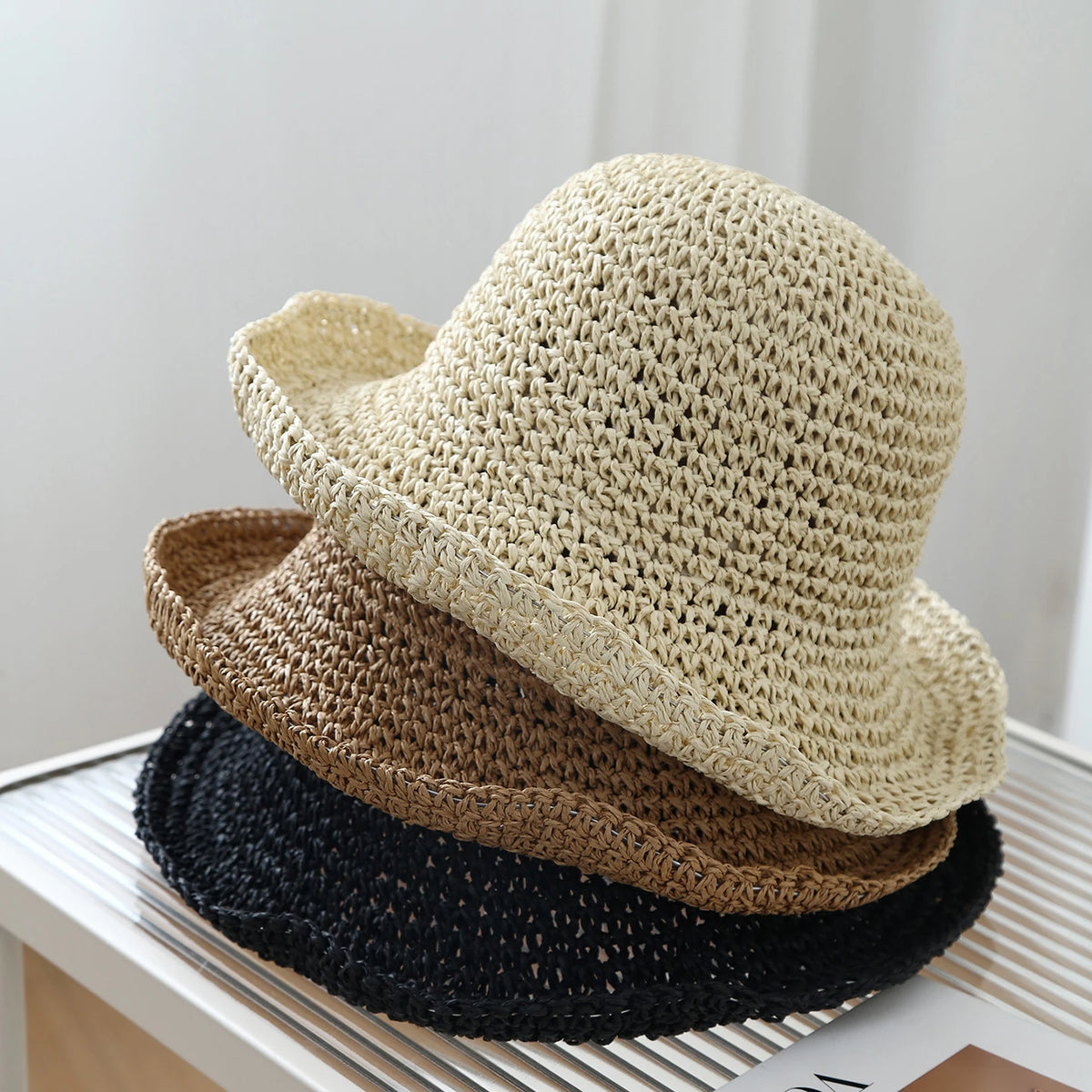 A beige crochet straw fisherman hat is stacked on a stack of brown and black hats.