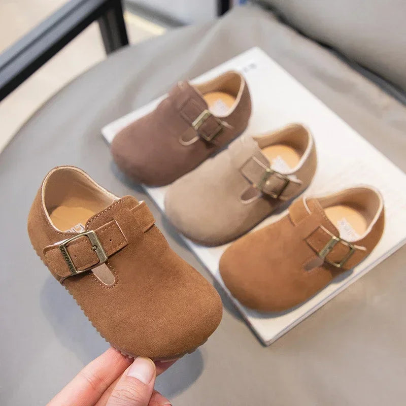 A pair of brown suede kids' moccasin shoes with tan lining and hook-and-loop closures displayed on a white surface.