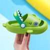 A hand holds a lime green kids shark clog sandal with a tooth-shaped accessory against a light blue background.