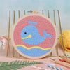 Kit de bordado con aguja circular, diseño de ballena azul y rosa sobre fondo claro.